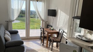 Una sala de estar con sofá, una mesa de comedor con sillas, televisor y una cocina con refrigerador y estufa.