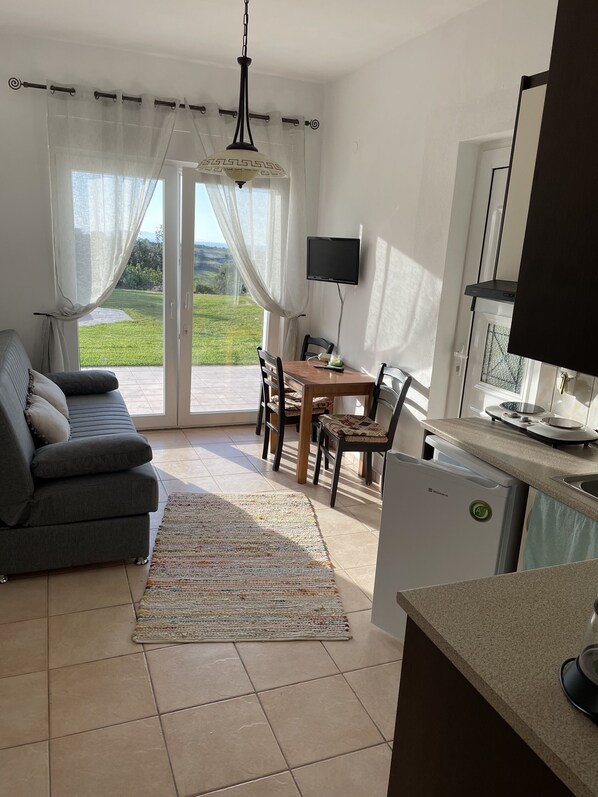 Una sala de estar con sofá, una mesa de comedor con sillas, televisor y una cocina con refrigerador y estufa.
