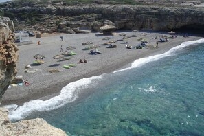 A beach with clear water, umbrellas, and people.