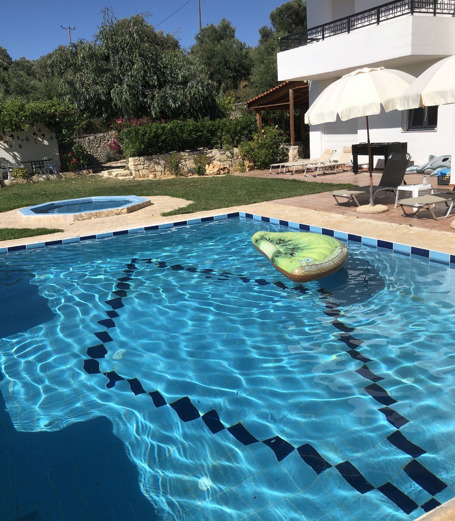 Une piscine avec une eau d’un bleu limpide, un flotteur gonflable vert et un parasol blanc.