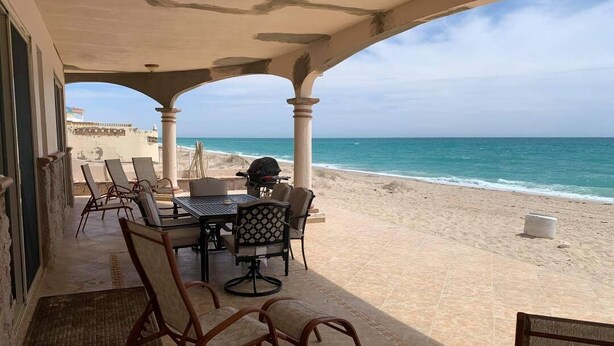 A covered outdoor seating area with a table and chairs, overlooking a beach.