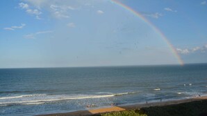 Une plage avec un arc-en-ciel, une mer calme et des gens qui profitent du bord de mer.