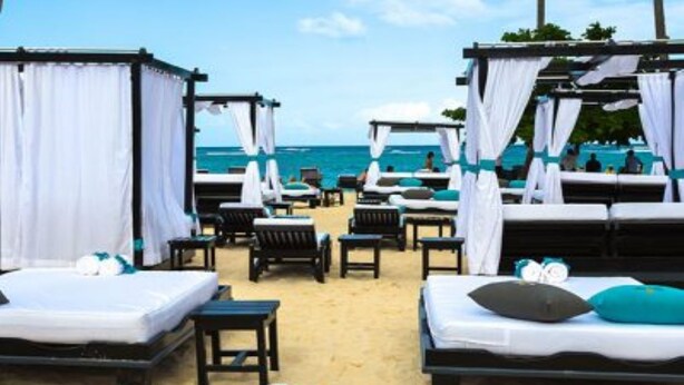 Habitación de hotel frente a la playa con dos camas, una mesita y una silla.
