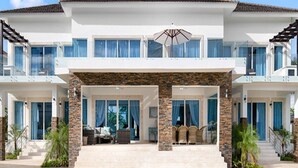 Una casa de dos pisos con un porche cubierto, amplias ventanas y un patio con mobiliario exterior.