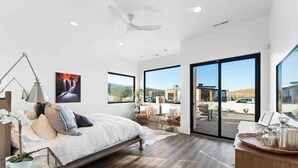 A modern bedroom with a bed, a desk, and a large window.