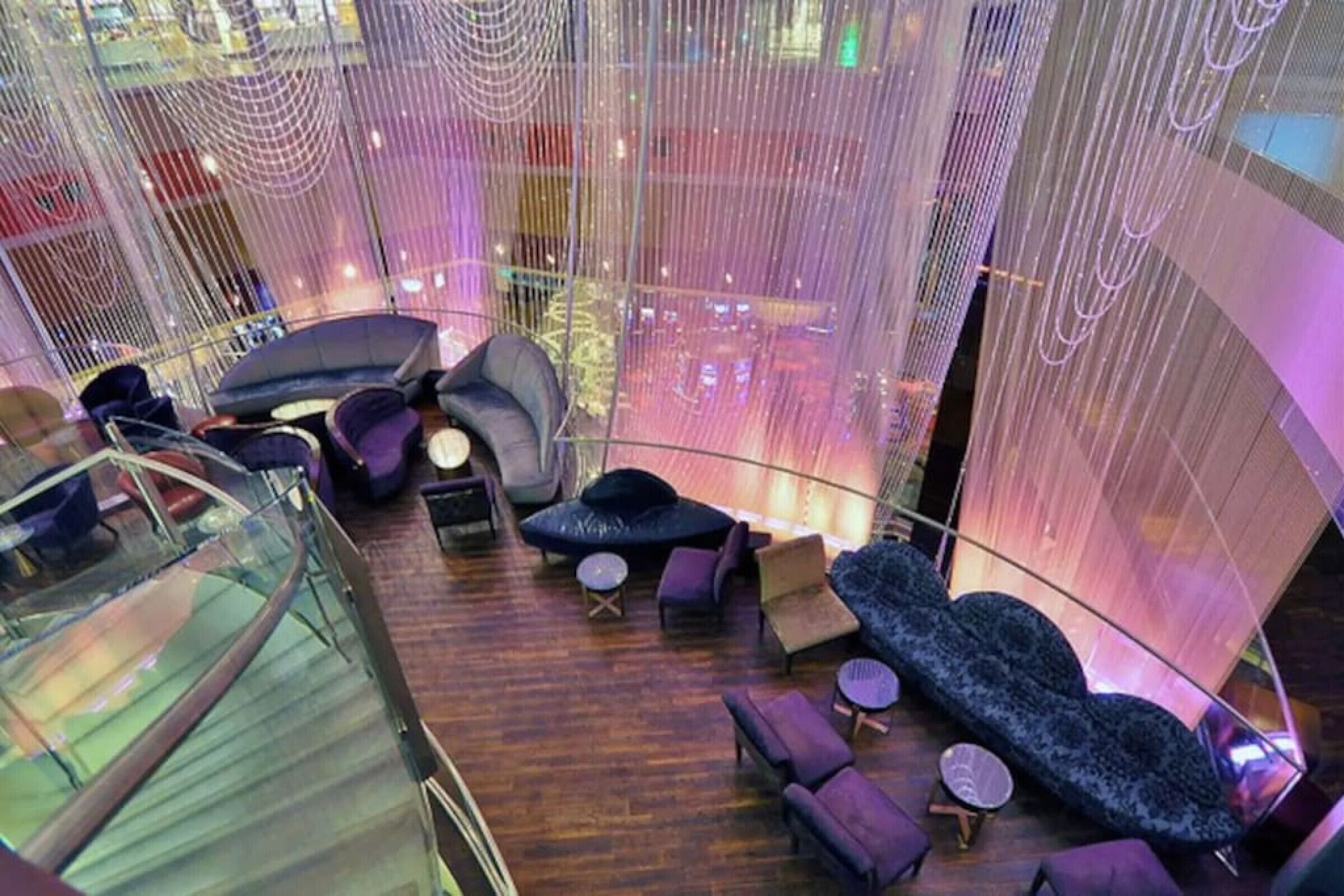 A modern interior with a glass railing, seating areas, and a view of the cityscape.