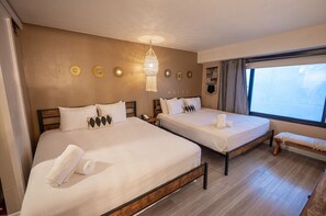 Une chambre d’hôtel avec deux lits, un banc, une grande fenêtre et des éléments de décoration murale.