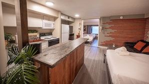 Une chambre d’hôtel moderne dotée d’une kitchenette, d’un lit recouvert d’une couette blanche et offrant une vue sur la chambre adjacente.