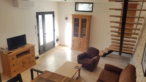 Ein Wohnzimmer mit Fernseher auf einer Holzkassette, einem braunen Sessel, einem kleinen Tisch und einer Treppe mit Holzstufen.