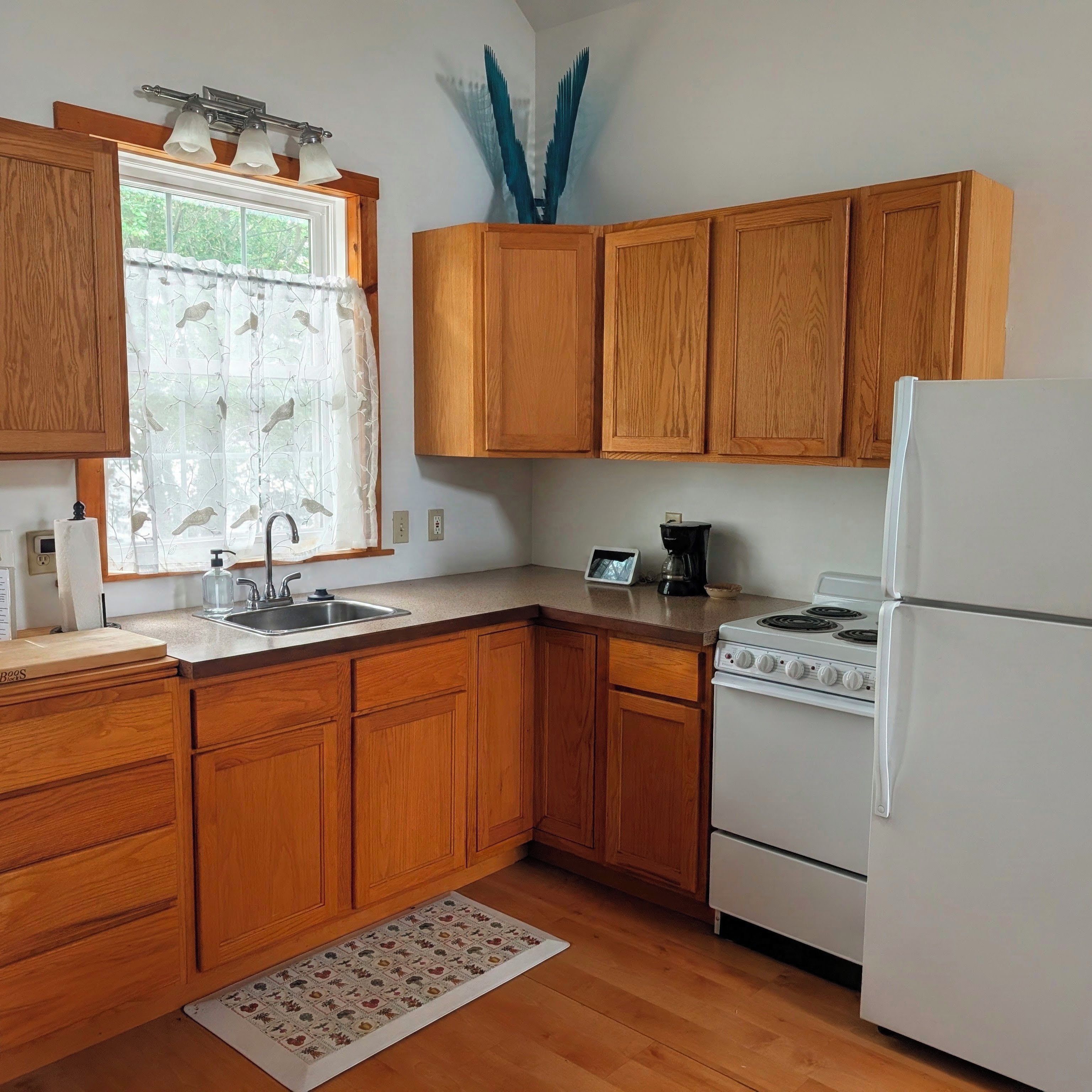 A kitchen with wooden cabinets, a white refrigerator, a stove, a sink, and a window with a curtain.