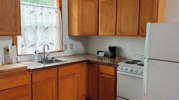 A kitchen with wooden cabinets, a white refrigerator, a stove, a sink, and a window with a curtain.