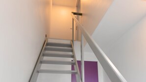 A modern staircase with a metal handrail and a purple door at the bottom.