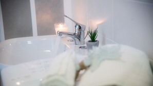 Une salle de bain avec une baignoire blanche, un robinet moderne, une bougie allumée et une petite plante en pot.