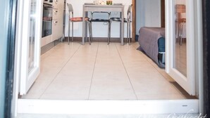 Une cuisine compacte dotée d’appareils électroménagers modernes, un coin repas avec une table et des chaises, et une vue dégagée par une porte ouverte.