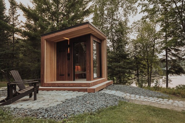 A small wooden cabin with a glass door, a bench outside, and a gravel path leading to it. - Northern Experience awaiting your adventure! (Orr)