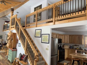 A spacious loft-style home with a wooden staircase, a kitchen with modern appliances, and a loft bedroom with a view.