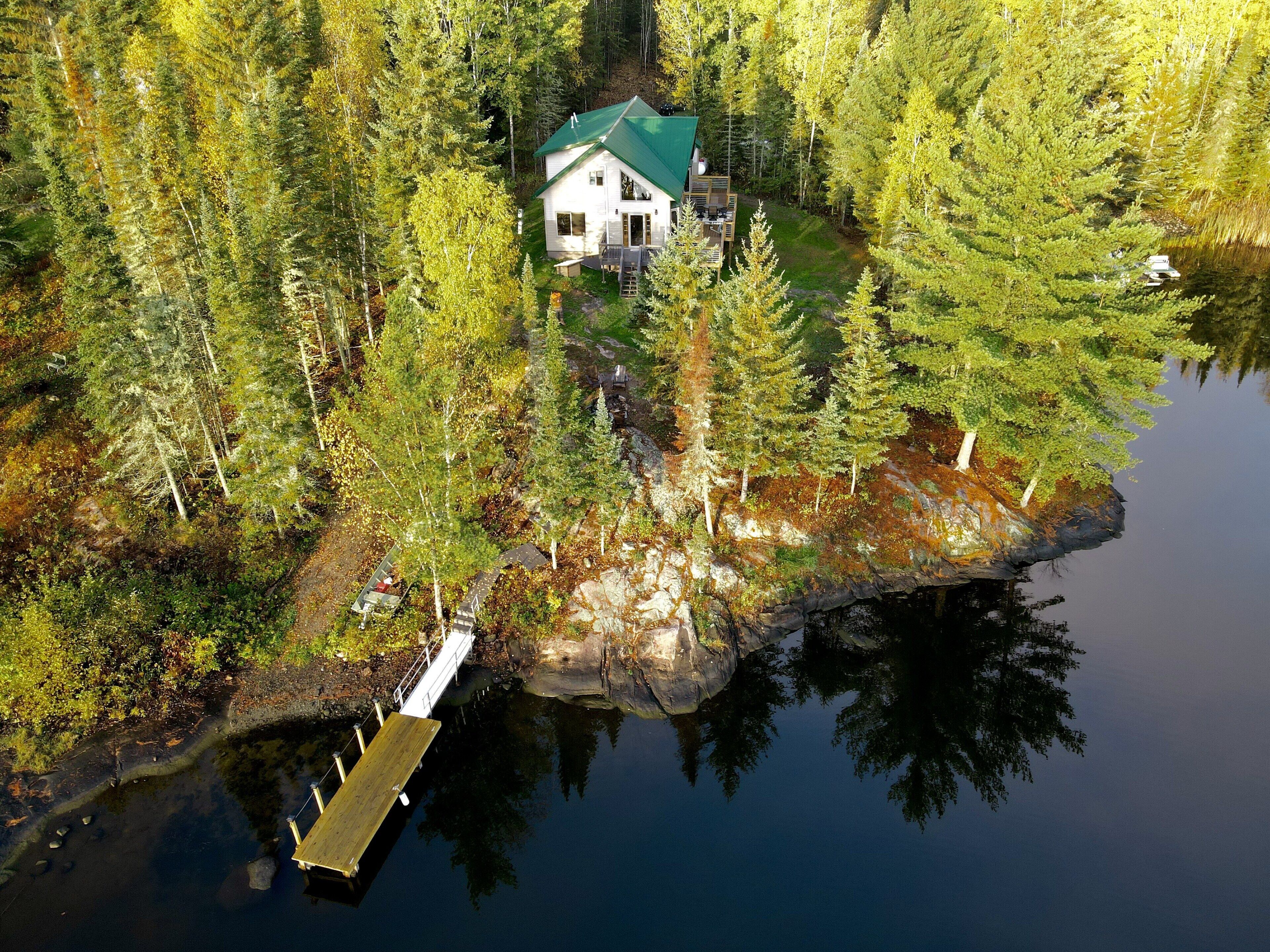 A house surrounded by dense forest, a dock, and a calm lake.