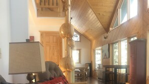 A spacious living room with a wooden ceiling, a large window, and a cozy seating area with a leather couch and a fireplace.