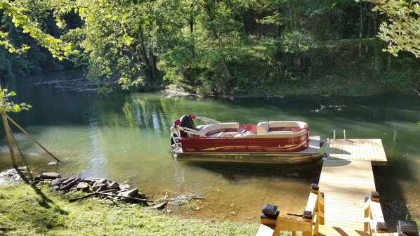 A boat docked at a wooden pier with a grassy bank and trees in the background.