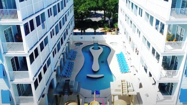 A multi-story hotel with a central swimming pool, balconies, and outdoor seating.