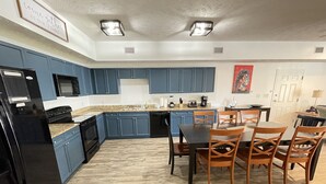 A kitchen with blue cabinets, a black refrigerator, and a dining area with wooden chairs.