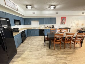 A kitchen with blue cabinets, a black refrigerator, and a dining area with wooden chairs. - Hum-Dinger, pool, lazy river & 2 hot tubs, Family friendly, 200yards to beach! (Myrtle Beach)