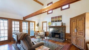 A spacious living room with a stone fireplace, wooden beams, and large windows. - Rustic, Private, Cozy Cabin Getaway in Mountains of Big Canoe (Big Canoe)