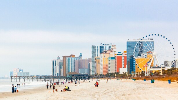 Een strand met een reuzenrad en hoge gebouwen op de achtergrond.
