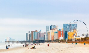Uma praia com uma roda gigante e edifícios altos ao fundo.