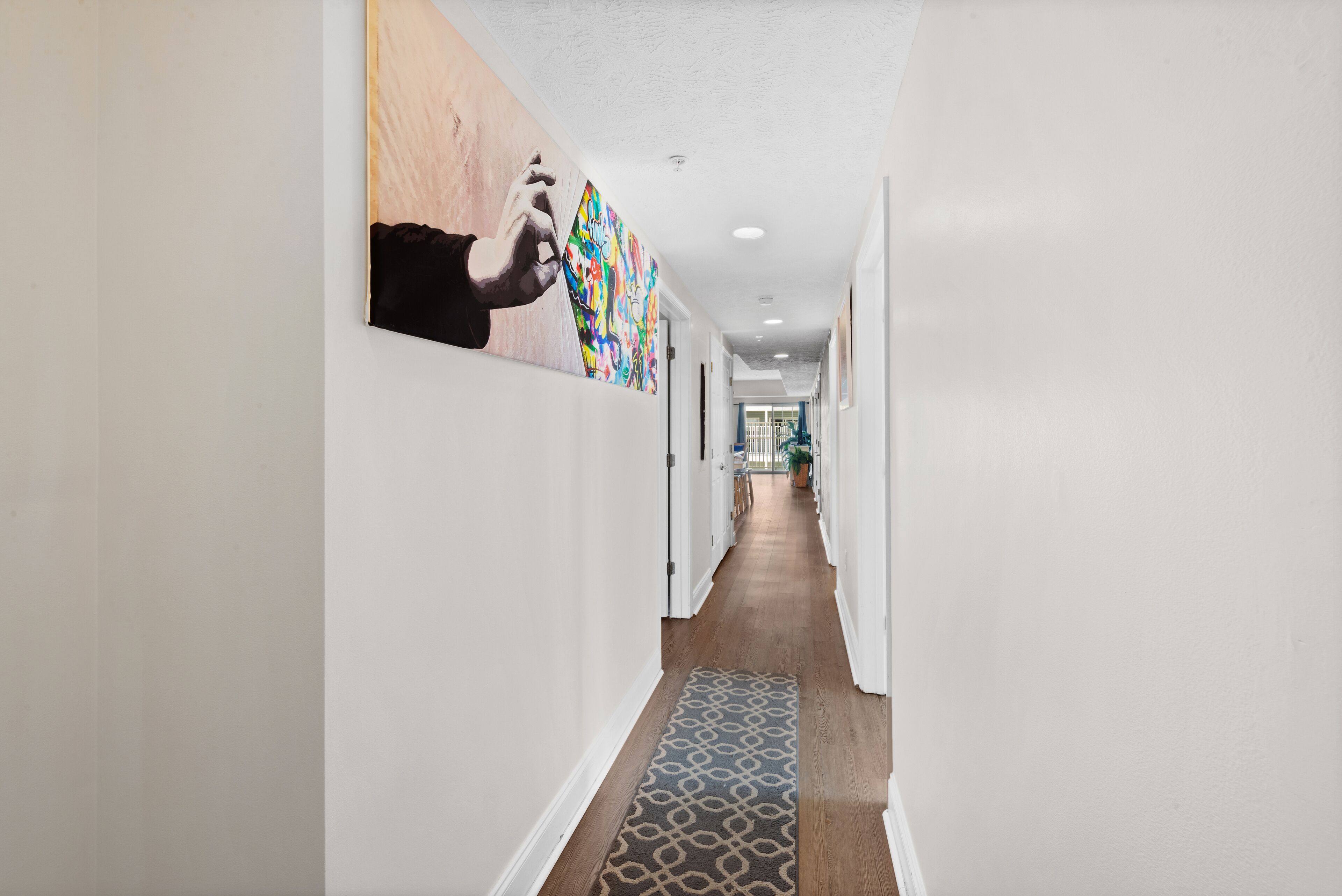 A hallway with white walls, a patterned rug, and colorful artwork.