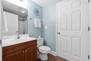 A bathroom with a white sink, wooden vanity, white toilet, and a white door. - Cloud 9-er (Myrtle Beach)