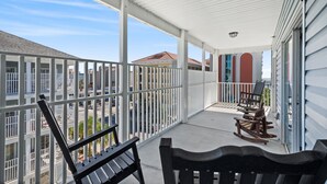 Een overdekt balkon met witte balustrades, twee houten schommelstoelen en een bankje.