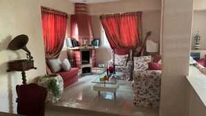 A living room with a fireplace, red curtains, a coffee table, and floral-patterned furniture. - Villa 100m from the beach (Mohammedia wilaya de Casablanca)
