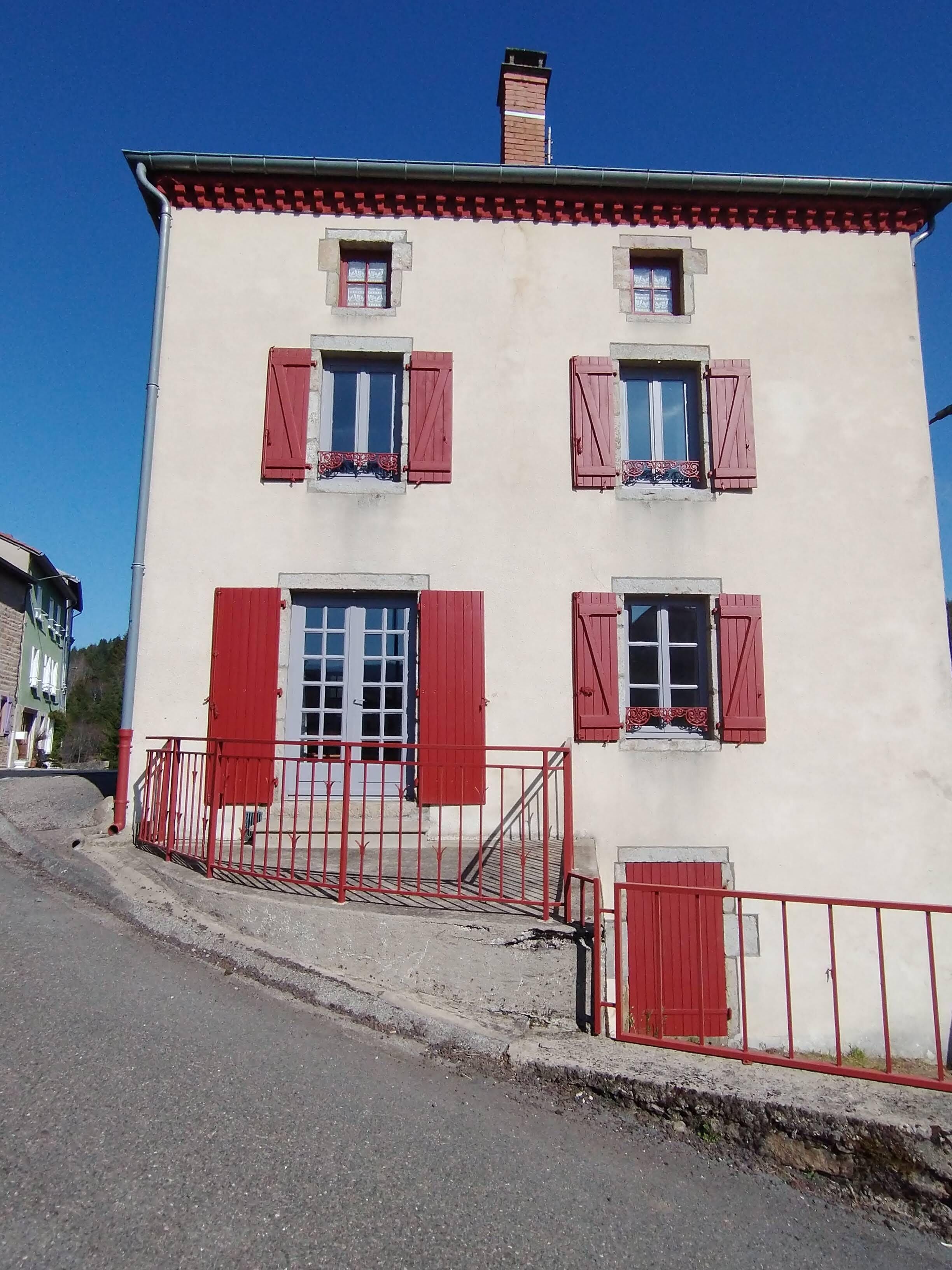 Un edificio de dos pisos con contraventanas rojas y fachada blanca.