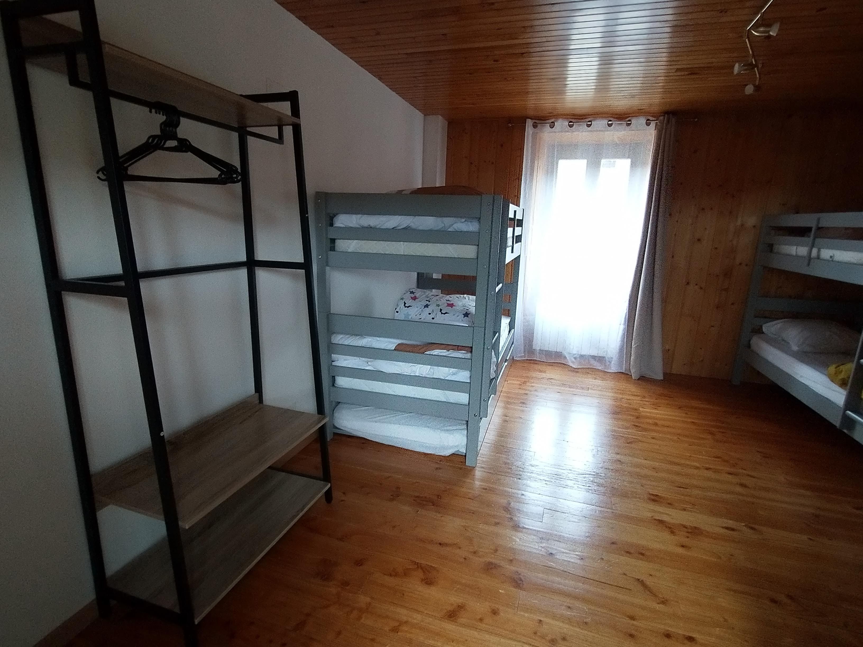 A room with bunk beds, a wooden floor, and a window with sheer curtains.