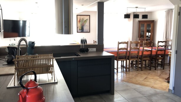 Een moderne keuken met een centraal eiland, houten stoelen, een eettafel en een groot raam.