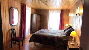 Een kamer met houten lambrisering, een bed, een stoel, een garderobe en een nachtkastje met een lamp.