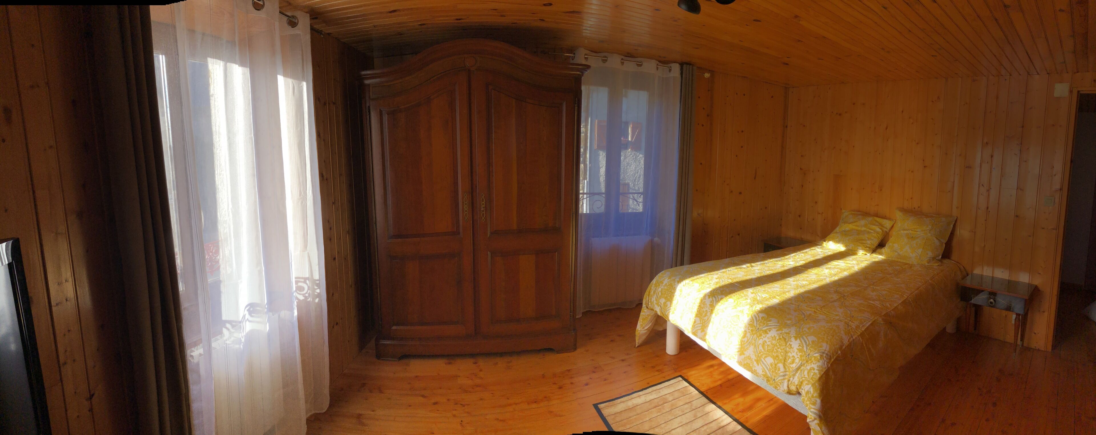 A wooden room with a bed, a wardrobe, and a window with curtains.