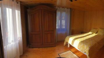 A wooden room with a bed, a wardrobe, and a window with curtains.