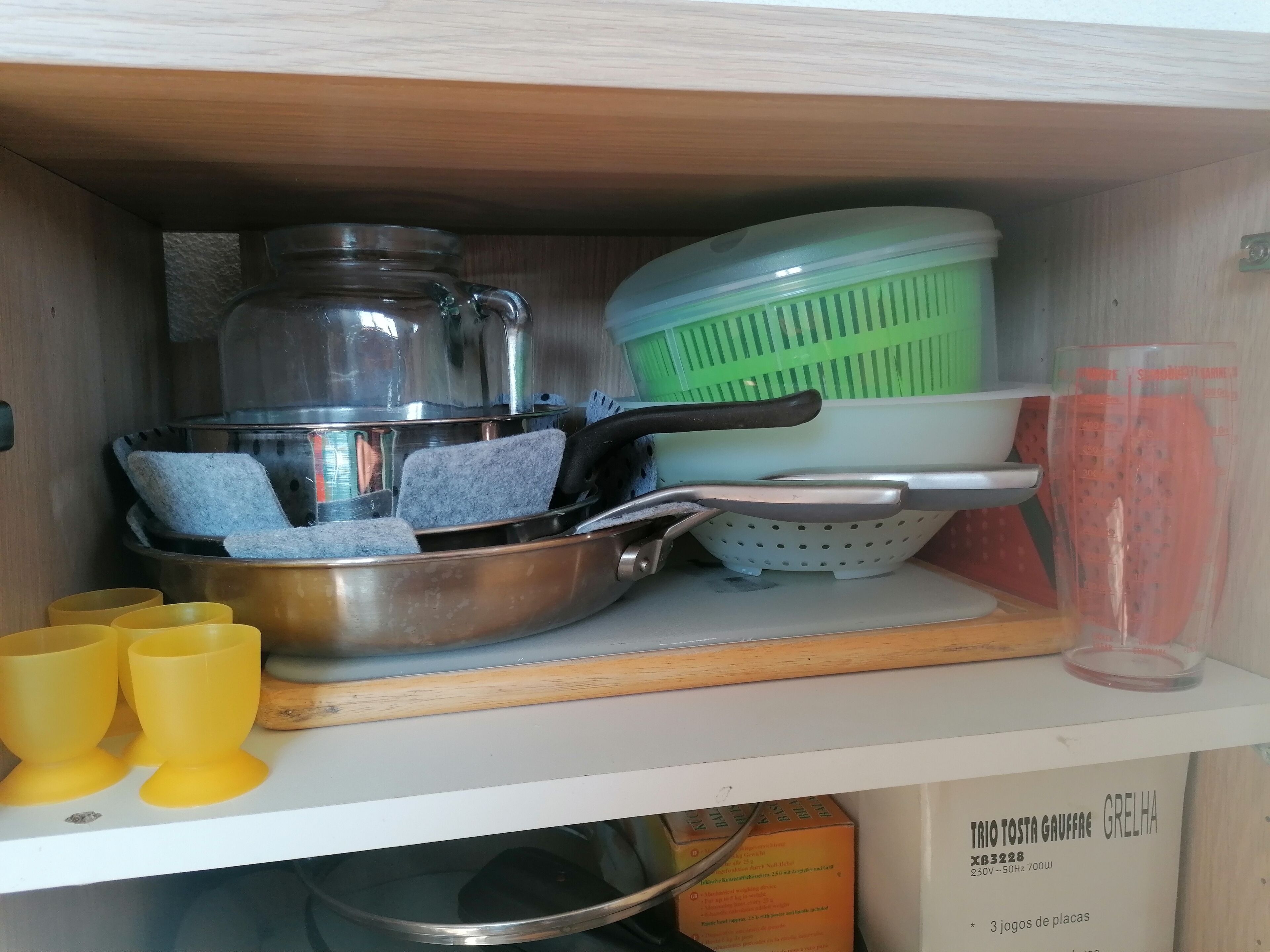 Un meuble de cuisine contenant divers ustensiles, notamment des casseroles, une passoire et des tasses jaunes.