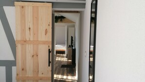 Een gang met een houten deur, een spiegel en een bed.
