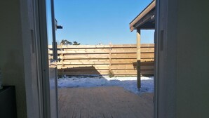 Een houten terras met een met sneeuw bedekte grond, een houten hek en een helderblauwe lucht.