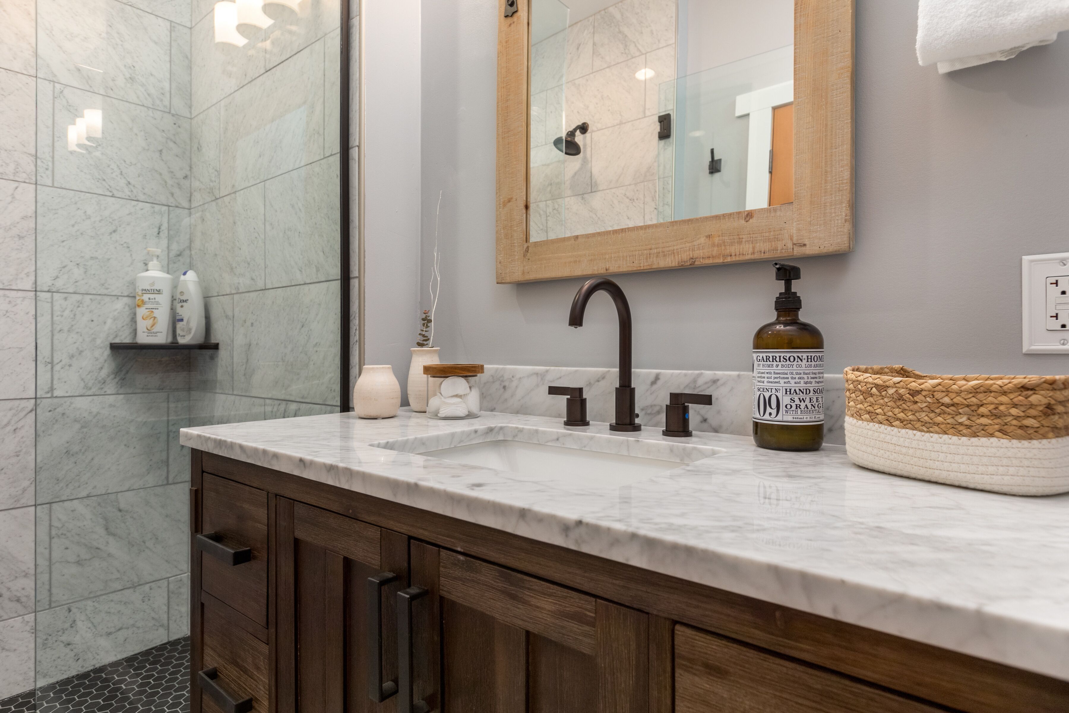 A bathroom with a marble sink, wooden cabinets, a mirror, and a shower area.