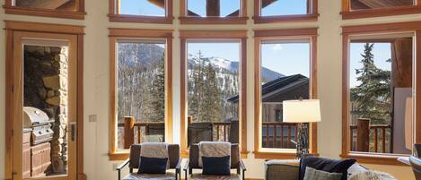 A spacious living area with large windows, a stone fireplace, and comfortable seating.