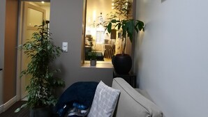Un salon avec un canapé, une grande plante en pot et un tableau encadré accroché au mur.