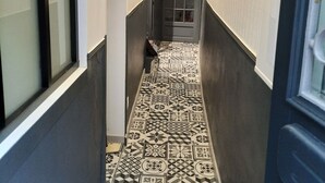 Un couloir étroit avec des carreaux de sol à motifs, une porte dotée d’un panneau de verre et un porte-manteau.