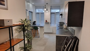 Une cuisine moderne avec un îlot central, un coin repas agrémenté d’une chaise verte et une grande fenêtre avec des stores.