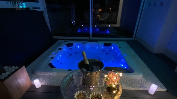Un bain à remous avec un éclairage bleu, une table décorée de bougies et une vue sur le ciel nocturne par une fenêtre.
