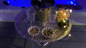Un bain à remous avec un éclairage bleu, une bouteille de champagne et deux verres posés sur une table, ainsi que des petits bols décoratifs remplis d’olives et de noix.