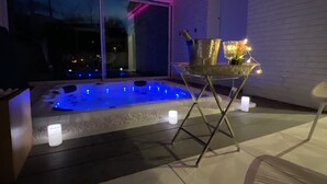 Une terrasse extérieure moderne dotée d’un jacuzzi, d’un éclairage d’ambiance et d’un espace repas avec une table et des chaises.
